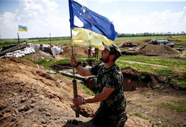 Український військовослужбовець тримає понівечений кулями прапор України на позиції біля міста Мар'їнка. Червень 2015 року
