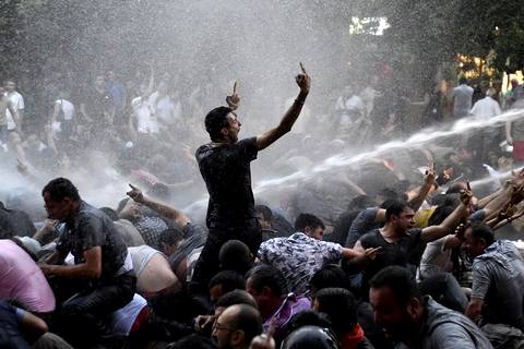 Protesters gesture as riot police vehicle sprays jet of water to disperse them during rally against recent decision to raise public electricity prices in Yerevan