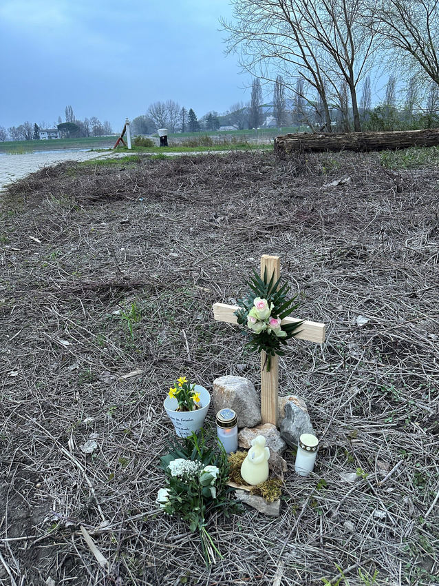 Цей дерев'яний хрест зі свічками і квітами стоїть на місці, де знайшли молоду жінку. Ліворуч так звана рампа НАТО, а з іншого боку Рейну купа сміття Шпаєр.