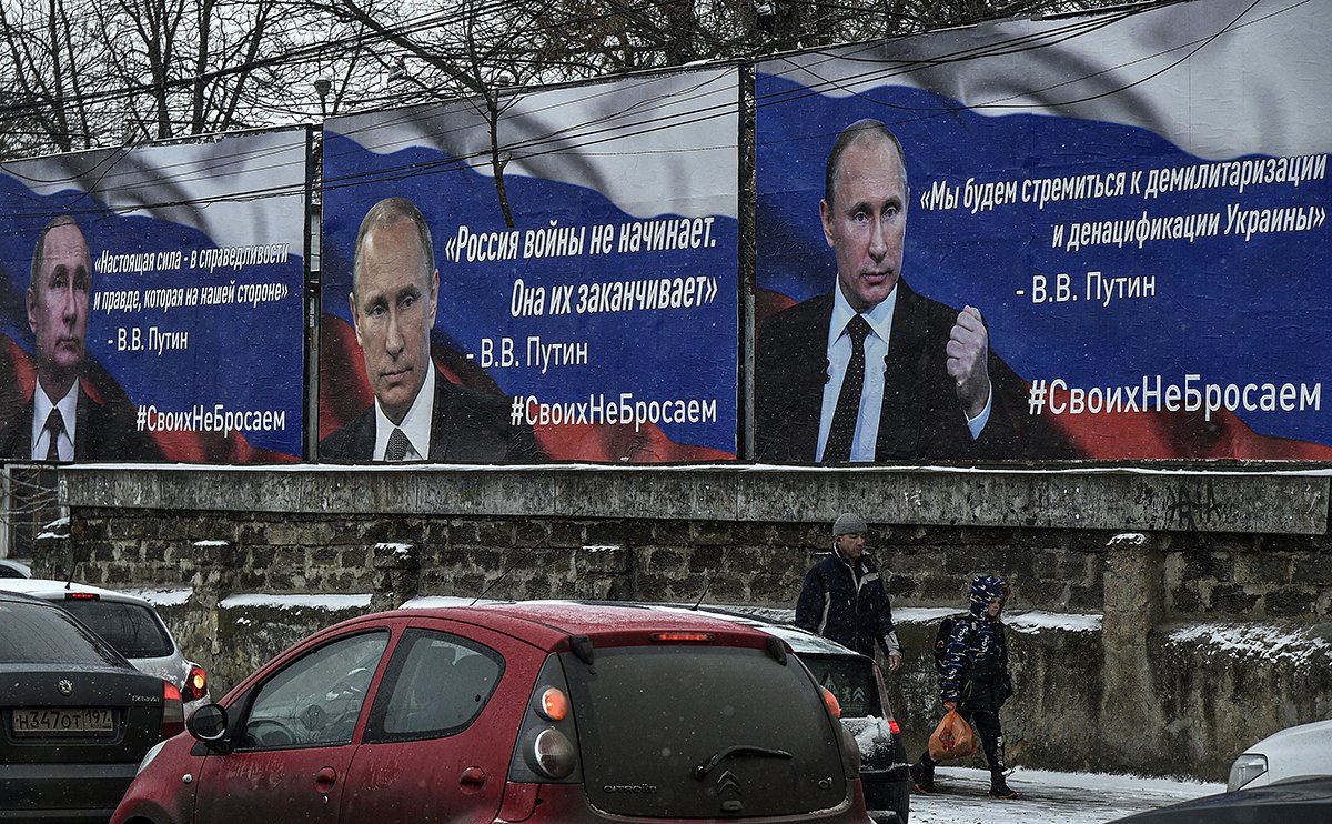 Местные жители проходят перед плакатами с портретами президента России Владимира Путина и милитаристскими лозунгами. Фото: EPA-EFE