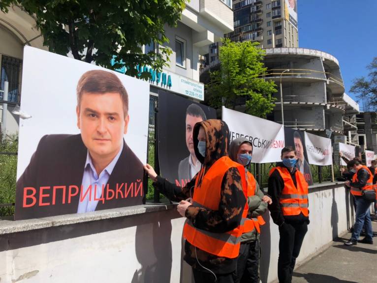 Участник митинга железнодорожников поправляет плакат с лицом Романа Веприцкого, которого обвиняли в коррупционных схемах. Киев, май 2020 года. Фото: aspi.com.ua Участник митинга железнодорожников поправляет плакат с лицом Романа Веприцкого, которого обвиняли в коррупционных схемах. Киев, май 2020 года. Фото: aspi.com.ua