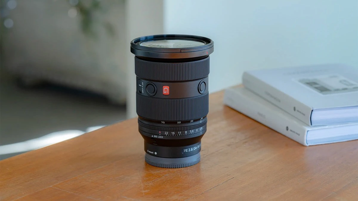 Об'єктив Sony FE 24-70mm f/2.8 GM II вертикально на дерев'яному столі з помаранчевим логотипом G, двома кнопками утримання фокусу та перемикачем Iris Lock