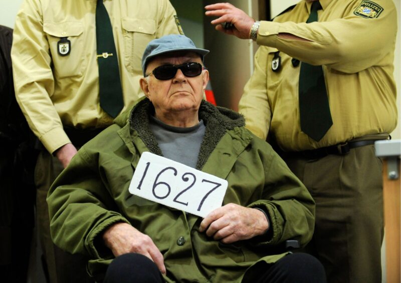 Джон Демьянюк держит табличку 1627 (номер советского следственного досье), в то время как его ввозят в зал суда в Мюнхене, Германия, 22 февраля 2011 года Фото: AP/Lukas Barth